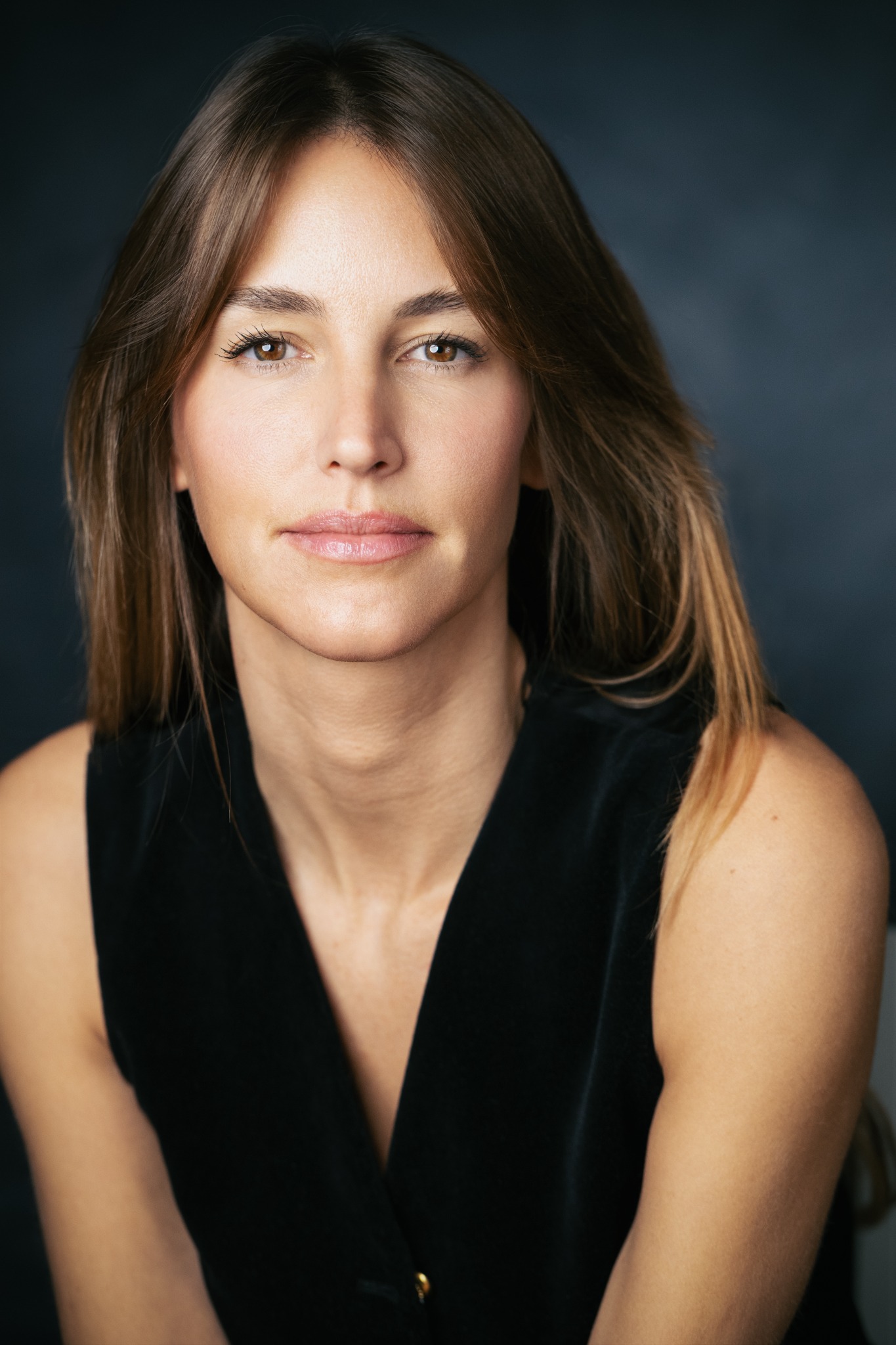 Headshot of actor Mariana Urbano, with brown hair and brown eyes, wearing a black top.